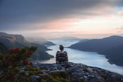 Rear view of woman looking at river amidst mountains against sky during sunset