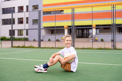 A boy holds a soccer ball while sitting on a soccer field