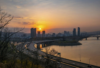 Bridge over river by buildings against sky during sunset