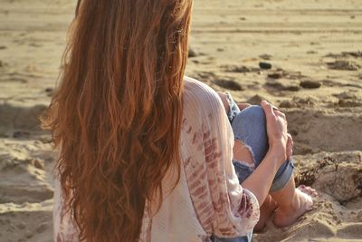 Rear view of woman with long brown hair sitting on sand at beach