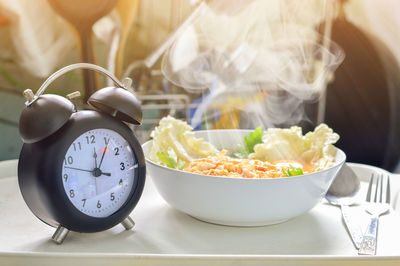 Close-up of food in bowl by alarm clock on table