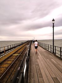 Rear view of girl walking on pier over sea against sky