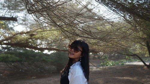 Young woman wearing sunglasses against trees at forest