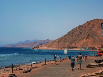 People on beach against clear blue sky