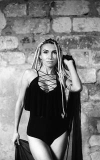 Portrait of young woman with dreadlocks standing against wall