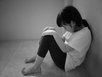 Rear view of woman sitting against wall at home