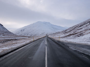 Empty road amidst snowcapped mountains against sky