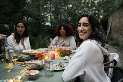 Portrait of smiling woman sitting on chair with friends at dinner party