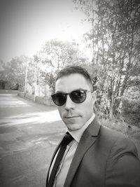 Portrait of young man wearing sunglasses standing against trees