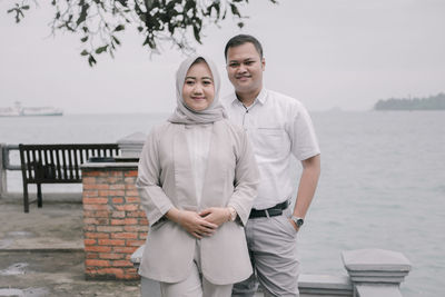 Portrait of smiling couple standing against sea