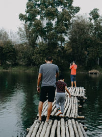 Rear view of men standing by lake against trees