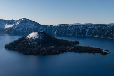 Scenic view of crater lake and wizard island against blue sky with snow