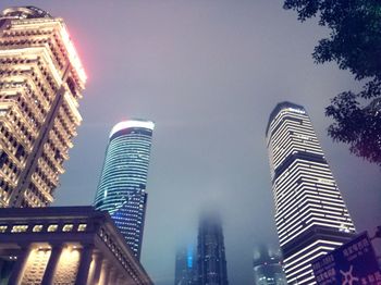 Low angle view of skyscrapers lit up against sky