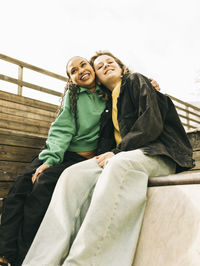 Smiling young woman embracing female friend while sitting on steps