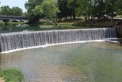 Scenic view of river flowing by trees against sky