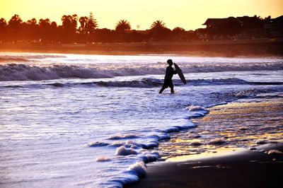 Silhouette man wading in sea against sky during sunset