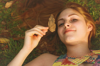 High angle portrait of young woman holding leaf while lying on field at park