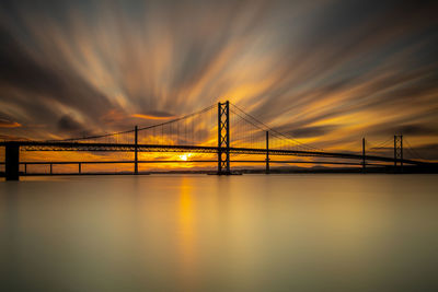 Suspension bridge over river against sky during sunset