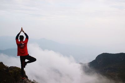 Rear view of man doing yoga on mountain against sky