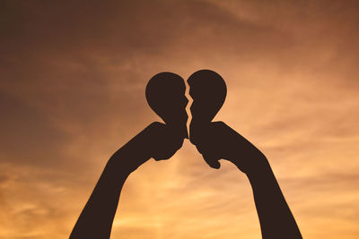 Cropped image of hands holding broken heart shape against dramatic sky