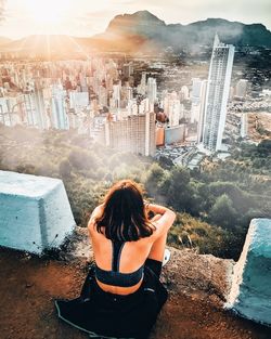 Rear view of woman sitting against buildings in city