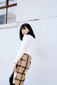 Portrait of smiling young woman standing against white wall