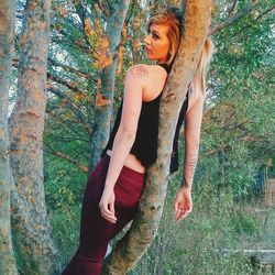 Woman with tattoo leaning on tree in forest