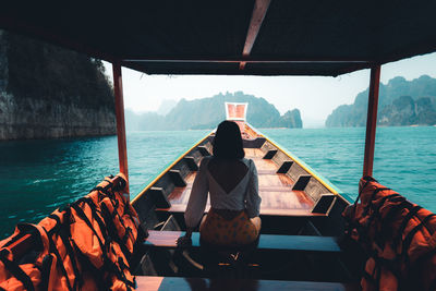 Rear view of people sitting on boat against sea