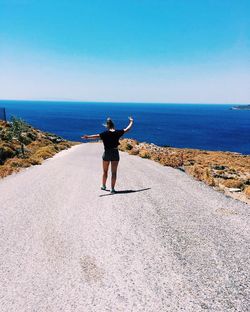 Rear view of woman standing on road leading towards beach against clear sky