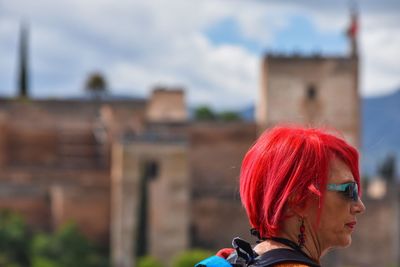Woman with red dyed hair looking away against historic building