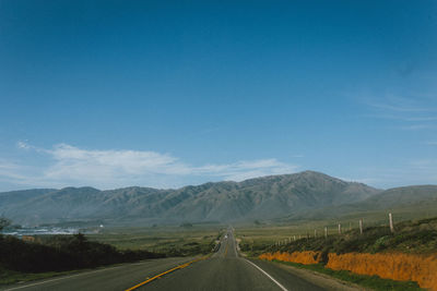 Empty road by mountains against blue sky