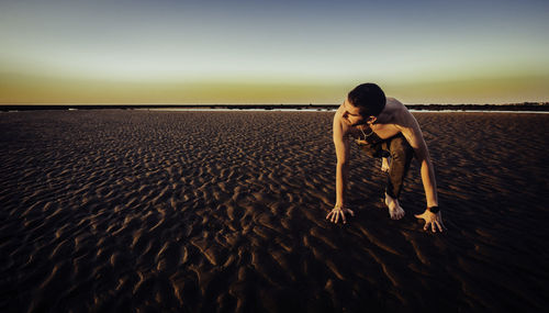 Shirtless man exercising on sand at beach against sky