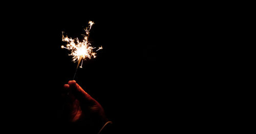 Cropped hand of woman holding sparkler against black background