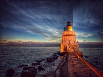 Lighthouse by sea against sky at sunset