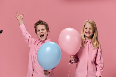 Happy boy and girl with balloon standing against wall