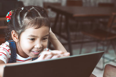 Smiling schoolgirl looking at laptop in classroom