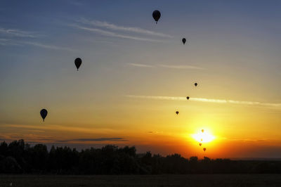Silhouette hot air balloons flying against sky during sunset