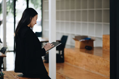 Portrait of young woman using digital tablet while standing in office