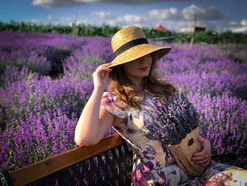 Portrait of woman wearing sun hat sitting down on a bench in a field of lavender