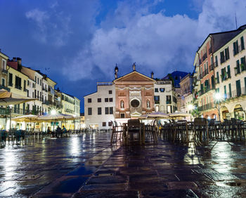 Wet street by buildings against sky in city