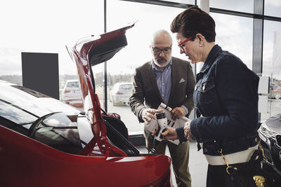 Senior man and woman examining charger of electric car at showroom