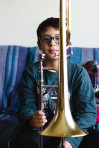 Portrait of cute boy holding trumpet while sitting on sofa at home