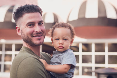 Dad holding baby boy, both looking at the camera