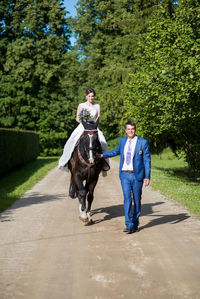 Bride with bridegroom riding horse on road during sunny day