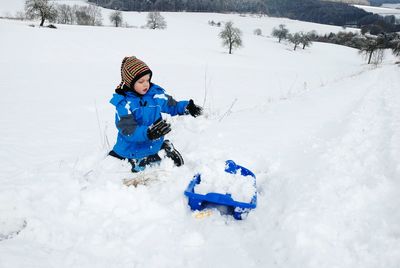 Cute boy playing on snow covered landscape during winter