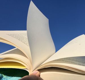 Low angle view of open book against blue sky