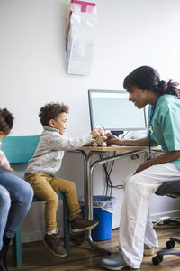 Boy talking to smiling female nurse while playing with stuffed toy in clinic