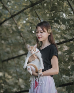Full length of woman holding pet against trees