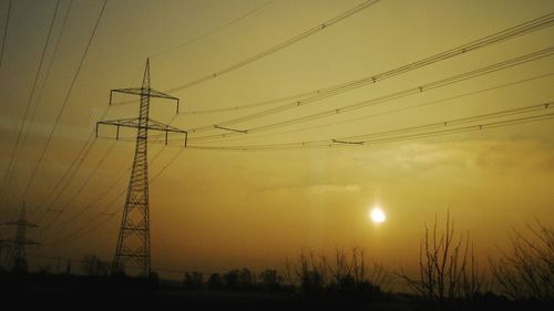 Low angle view of electricity pylon at sunset