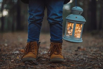 Low section of child with lantern standing in forest